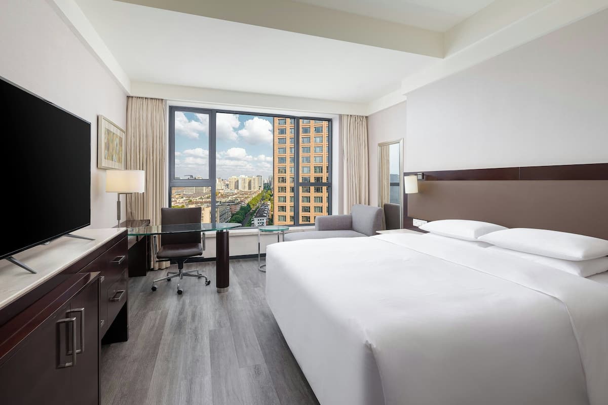 Une chambre d’hôtel avec un grand lit, un bureau avec une chaise, une télévision et une grande fenêtre donnant sur la ville.