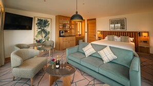 Ein Hotelzimmer mit Bett, Sofa, einem kleinen Tisch mit Flasche und Gläsern, Fernseher, Küchenzeile und Bildern an den Wänden.