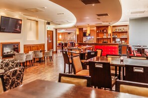 Un restaurante con suelo de madera, asientos rojos y una zona de bar con estantes llenos de botellas.