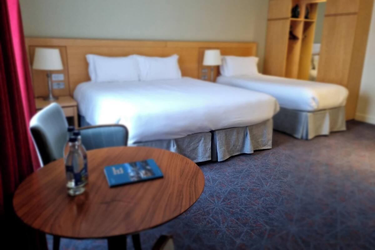 A hotel room with a large bed, a smaller bed, a desk with a chair, and a wardrobe.