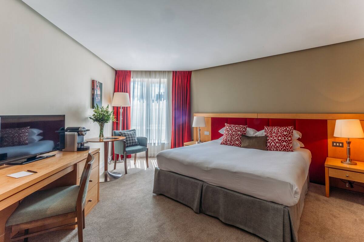 A hotel room with a bed, desk, chair, television, and a window with curtains.