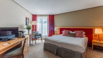 A hotel room with a bed, desk, chair, television, and a window with curtains.