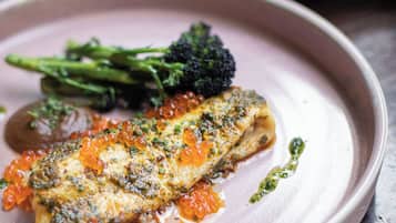 A plate with a piece of fish topped with roe, accompanied by broccoli and a sauce.