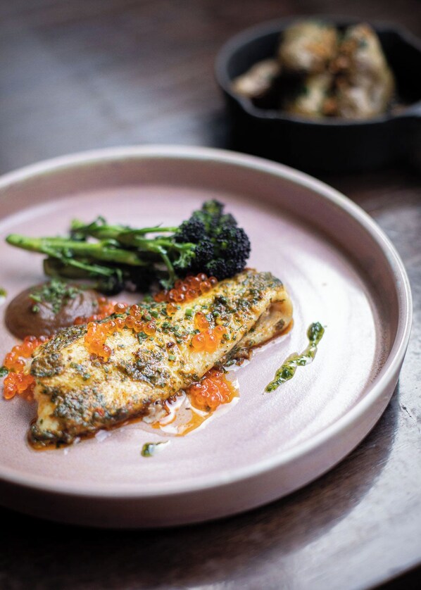 A plate with a piece of fish topped with roe, accompanied by broccoli and a sauce.