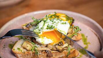 A plate with a poached egg, mushrooms, and greens on toast, with a fork and knife on the side.