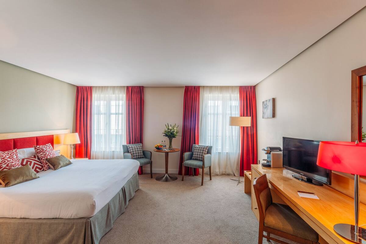 A hotel room with a bed, a desk, a TV, and two chairs.