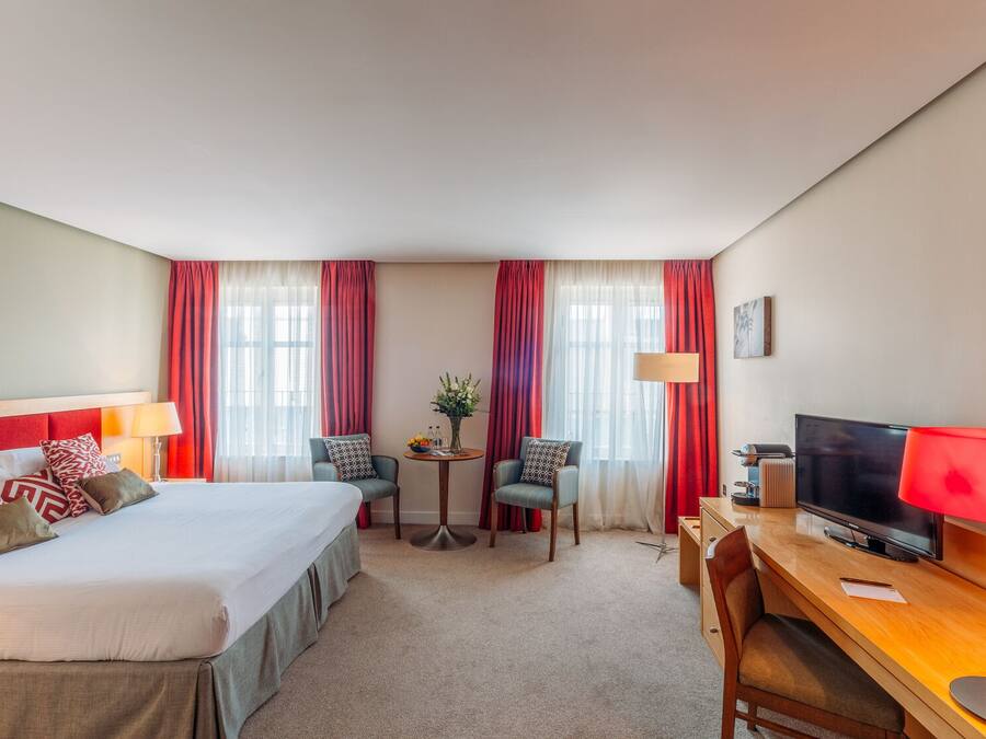 A hotel room with a bed, a desk, a TV, and two chairs.