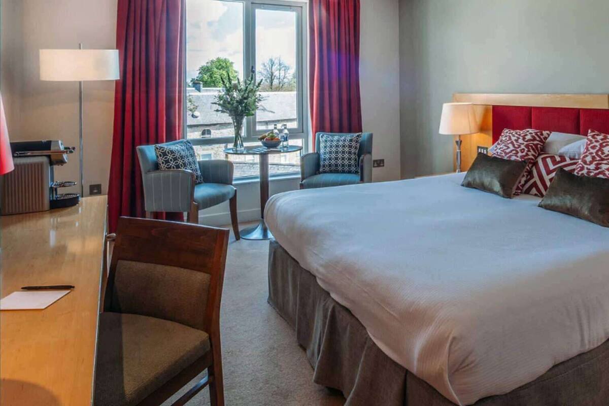 A hotel room with a large bed, two chairs, a small table, and a lamp.