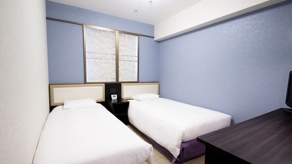 Une chambre d’hôtel avec deux lits, une petite table, une table de chevet et une fenêtre.