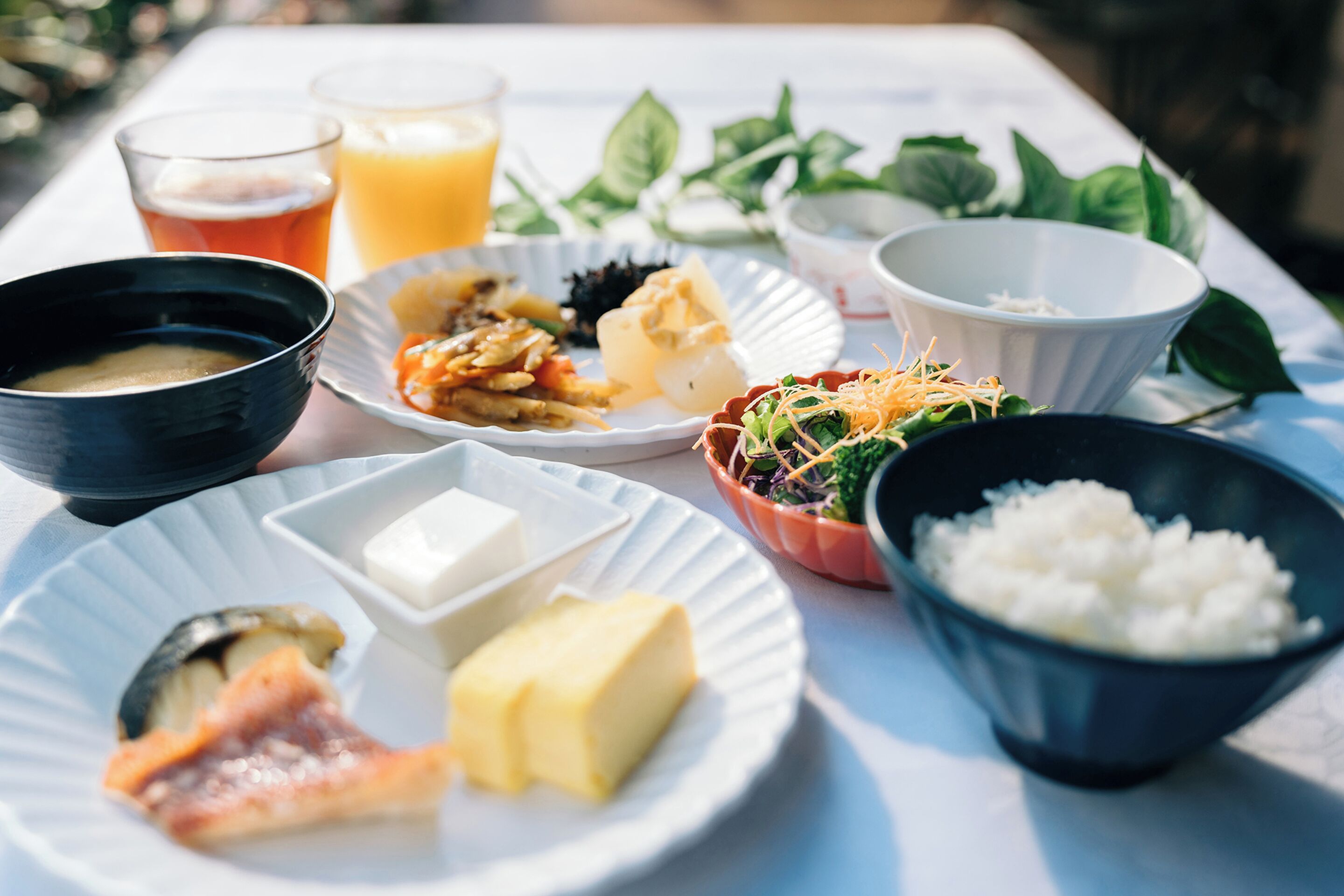 A table with various dishes including a bowl of soup, a plate with cheese and ham, a bowl of rice, and a glass of orange juice.