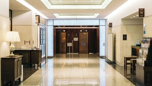 Een hotelhal met een gepolijste vloer, een receptiebalie en een trap die naar de liften leidt.
