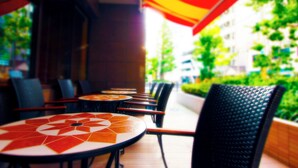 Een rij tafels met een geometrisch patroon in het midden, omringd door stoelen, onder een grote parasol.