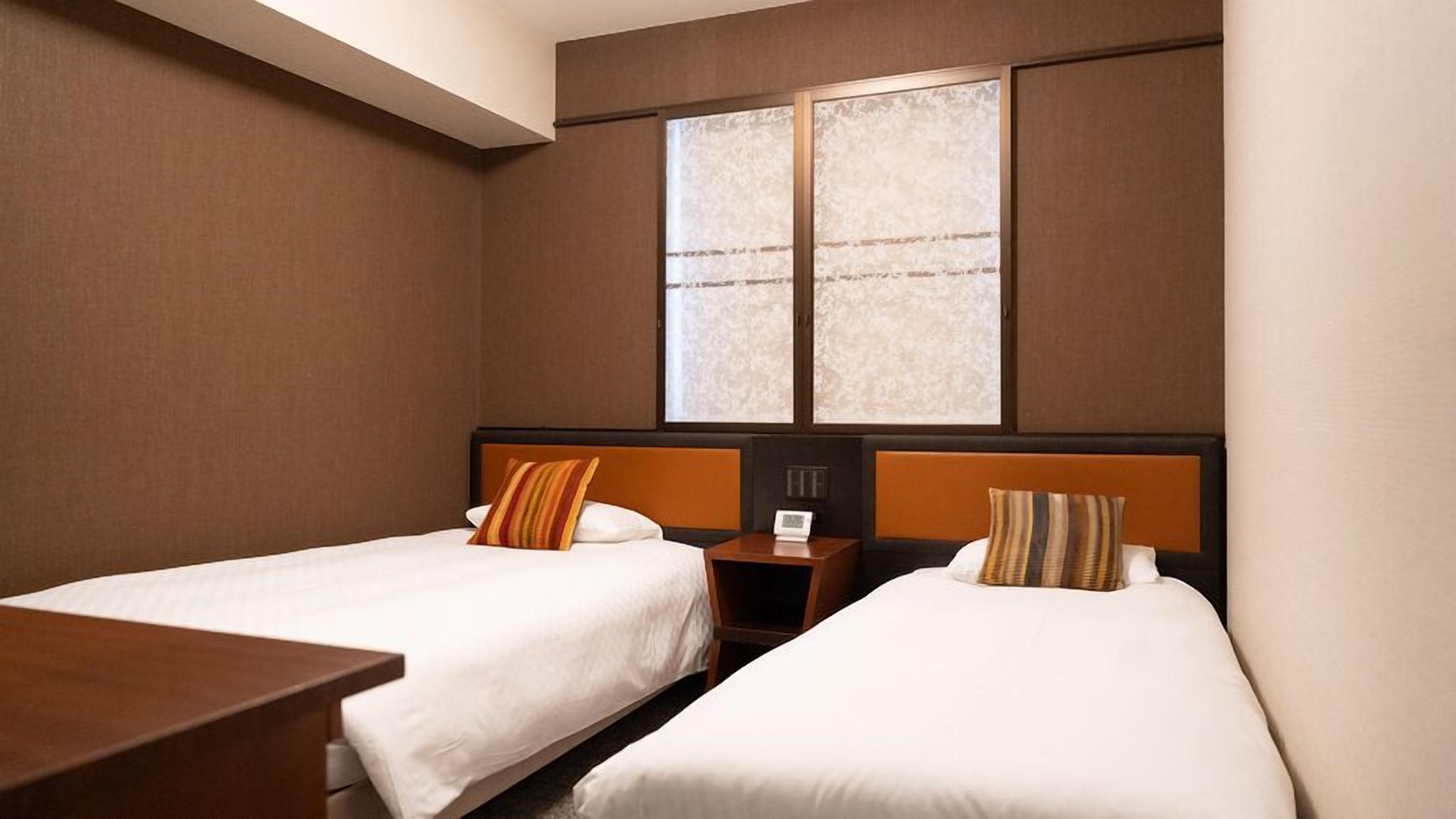 Une chambre d’hôtel avec deux lits, une table de chevet, un bureau et une grande fenêtre donnant sur un beau paysage.