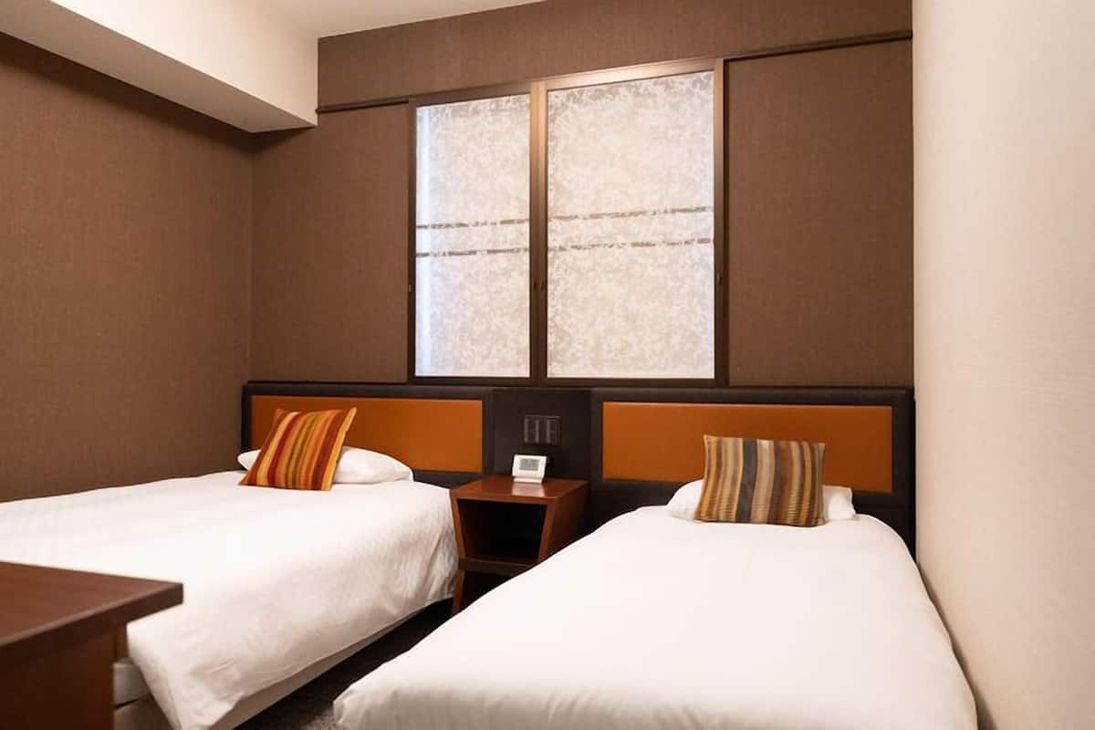 A hotel room with two beds, a nightstand, a desk, and a large window with a view.