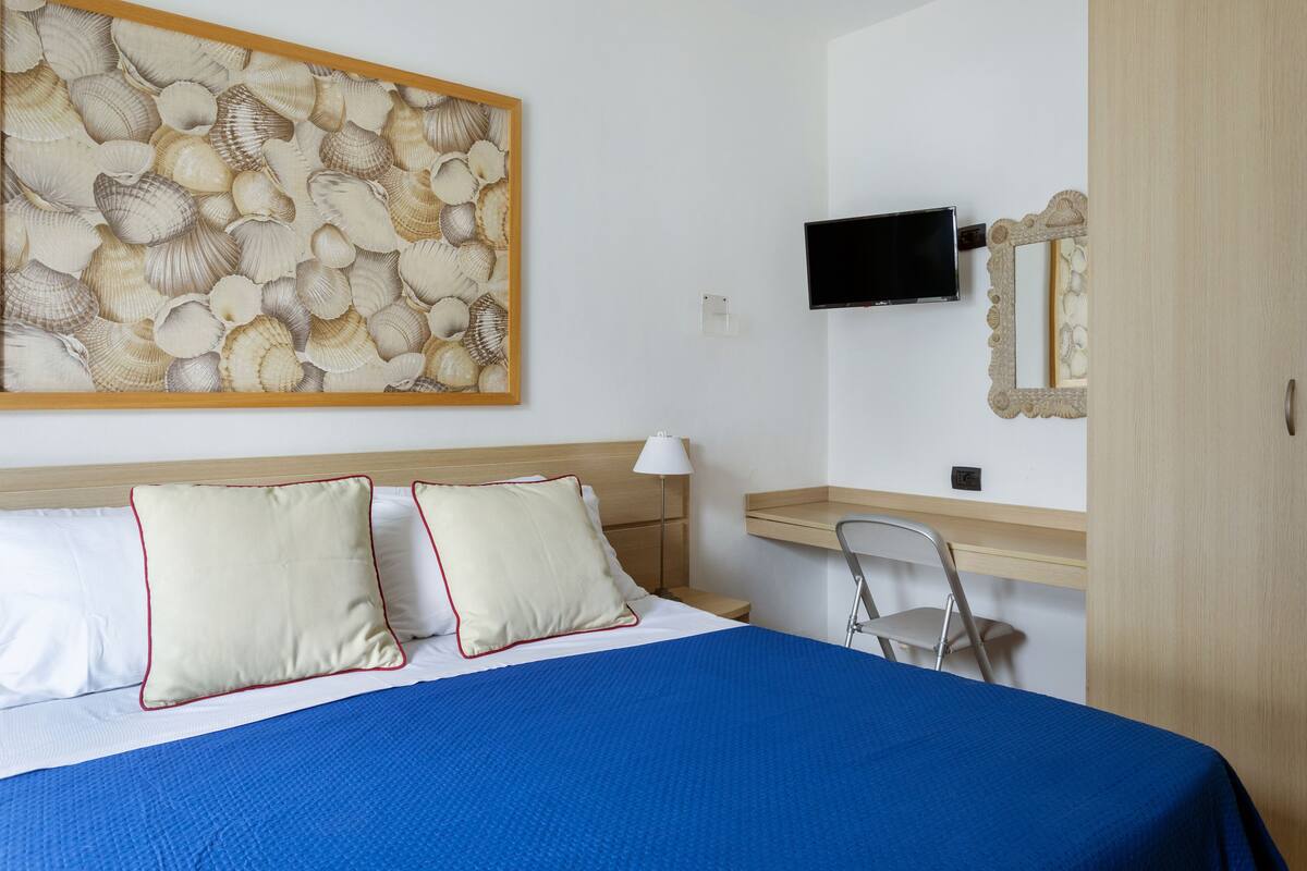 A hotel room with a bed, a desk, a chair, a television, and a wall-mounted mirror.