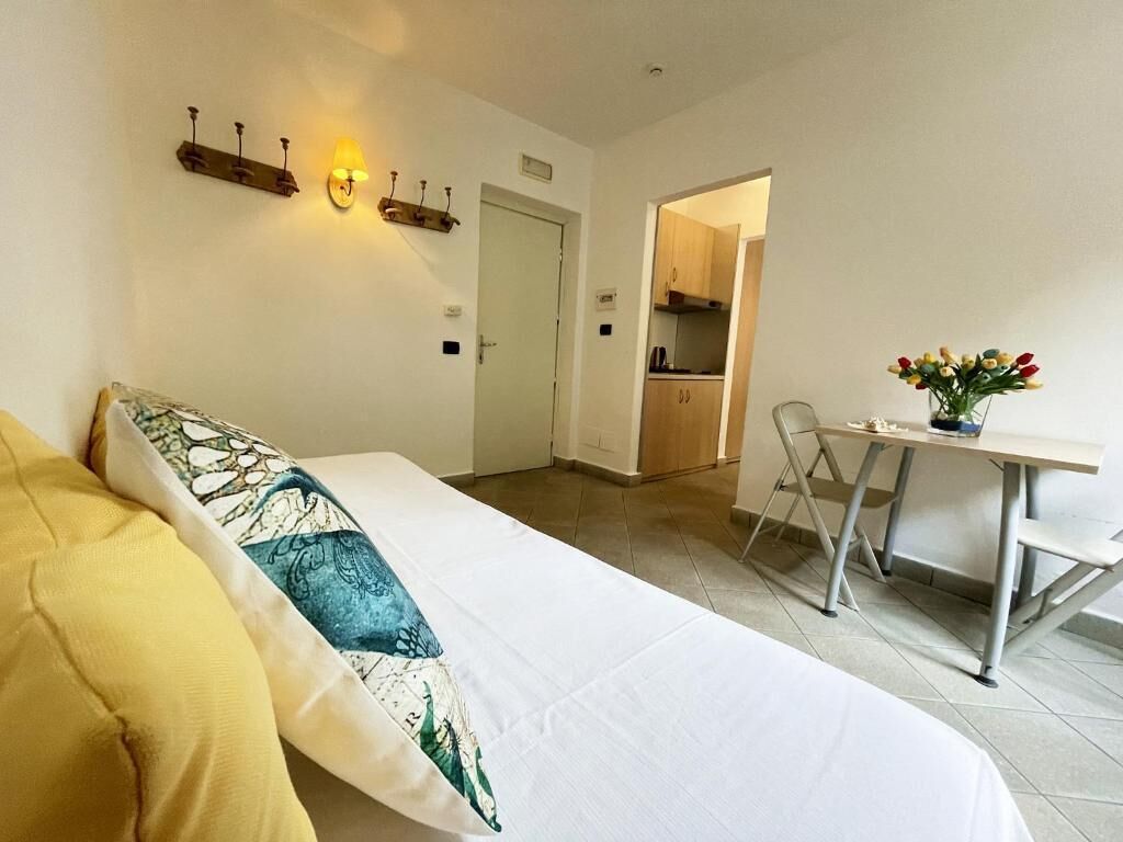 Une chambre d’hôtel avec un lit, un bureau et une chaise. On aperçoit un coin cuisine au fond de la pièce.