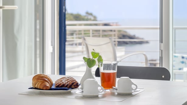 Une table avec des croissants, une tasse de thé et un vase blanc contenant une plante verte.