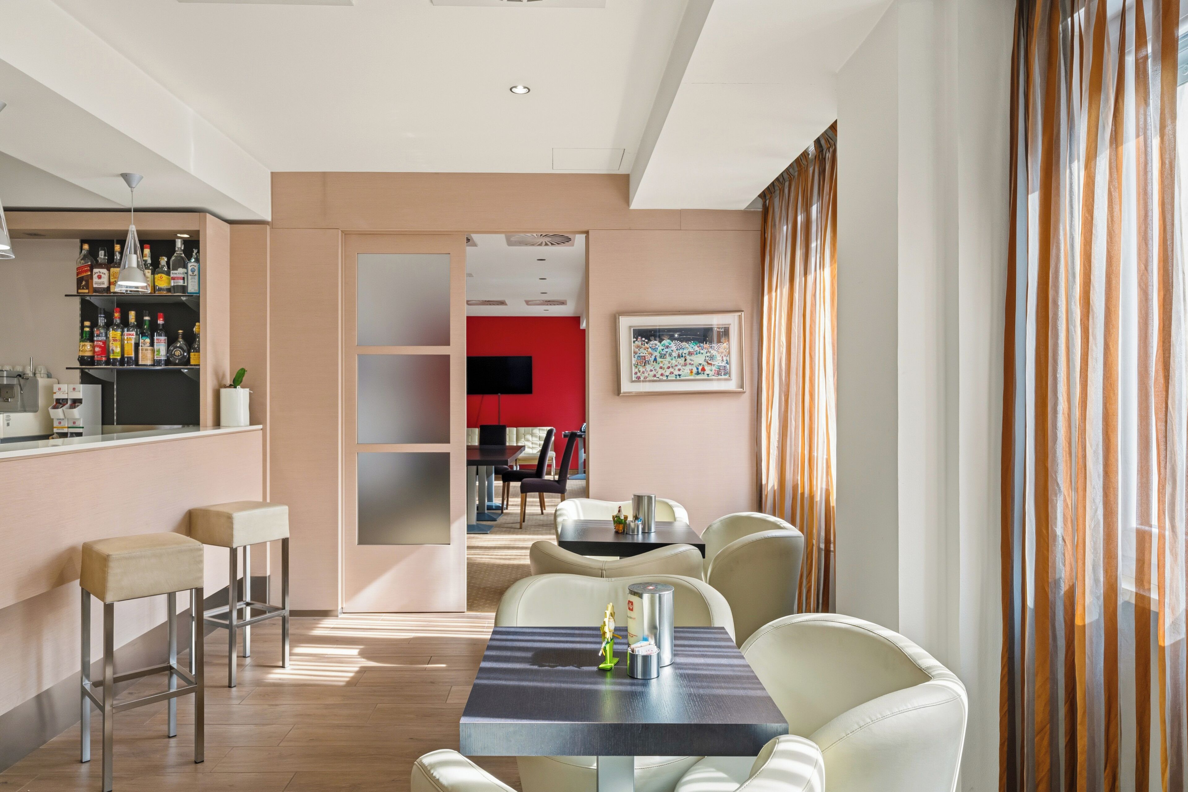 Et moderne hotelværelse med spiseplads, en bar med spiritusflasker og en rød accentvæg.