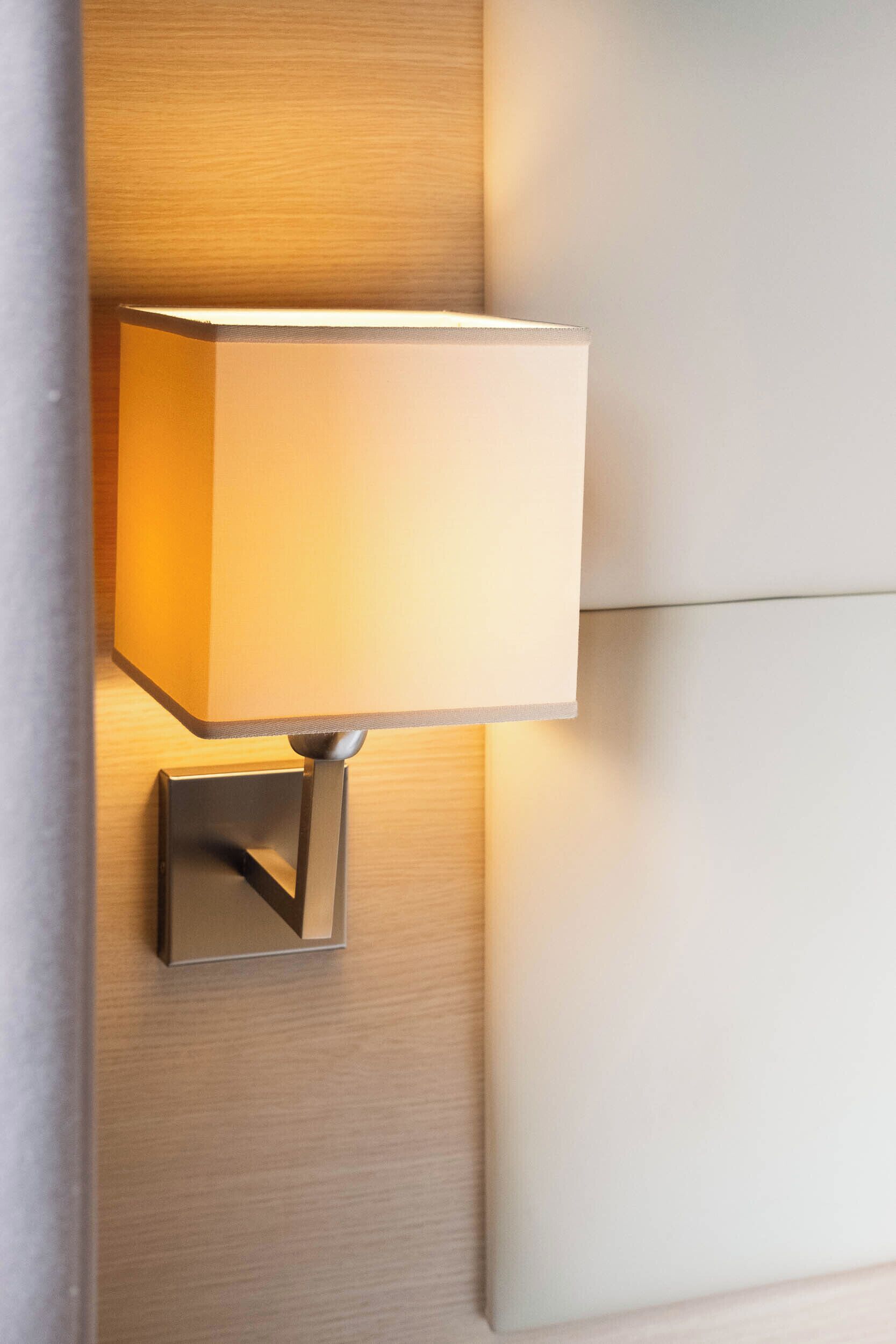 Eine Wandleuchte mit rechteckigem Lampenschirm und metallenem Fuß.