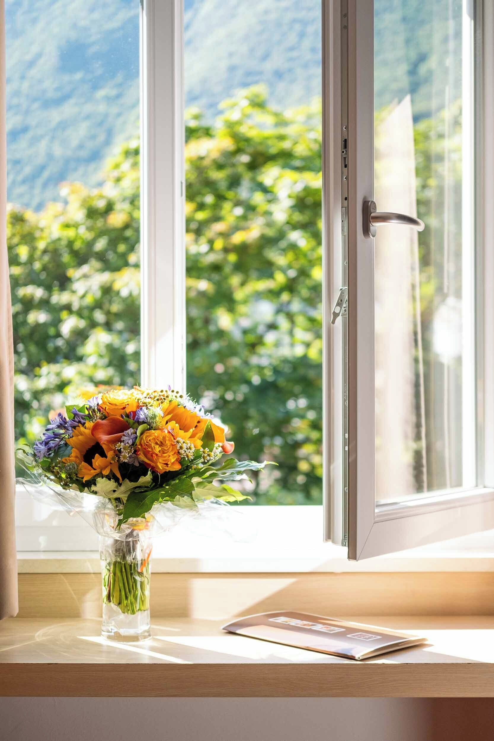A window with a view of greenery, a vase with flowers, and a closed door.