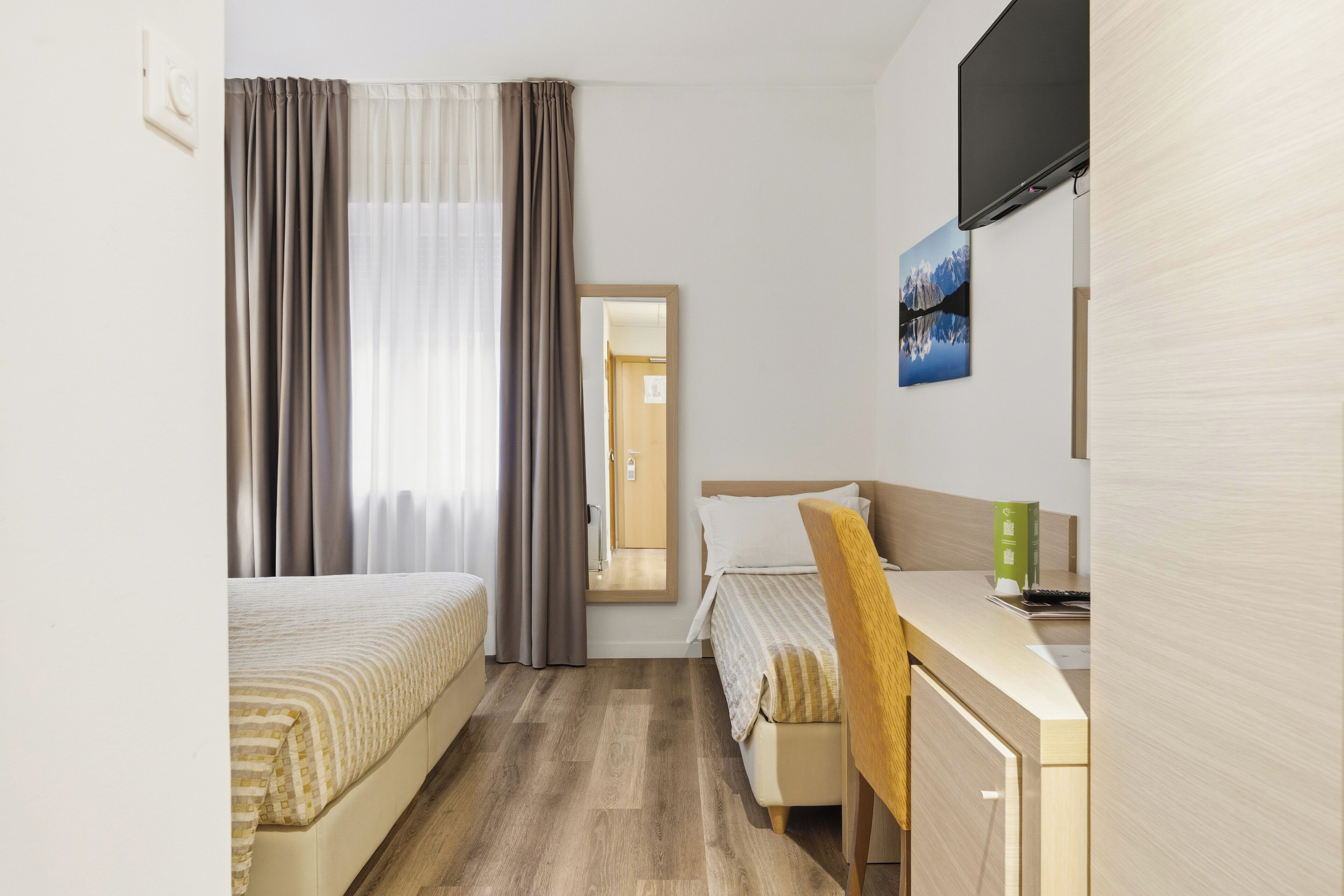 A hotel room with two beds, a desk, a TV, and a window with curtains.