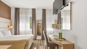 Una habitación de hotel con cama, escritorio, silla, televisor y cortinas.