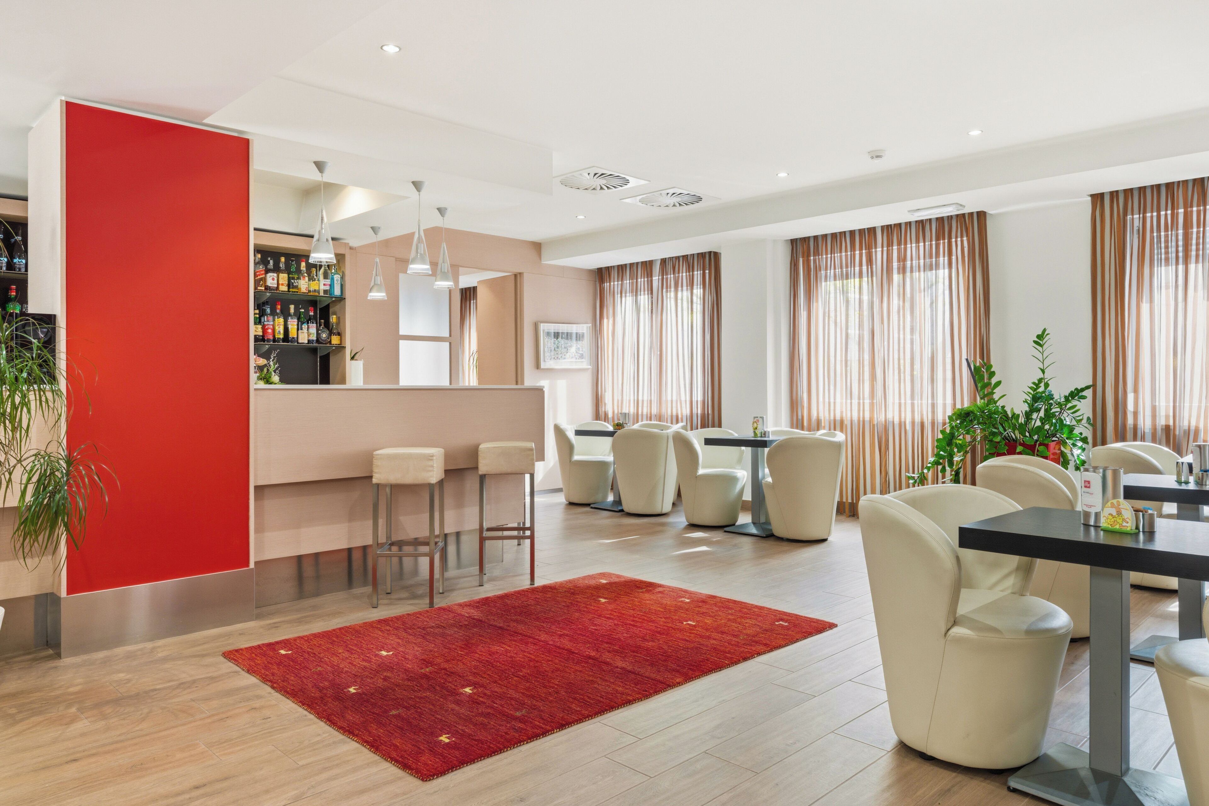 A modern hotel lobby with a bar, seating area, and a red accent wall.