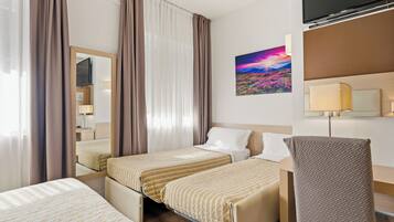 A hotel room with two beds, a TV, a painting, and a desk with a lamp.