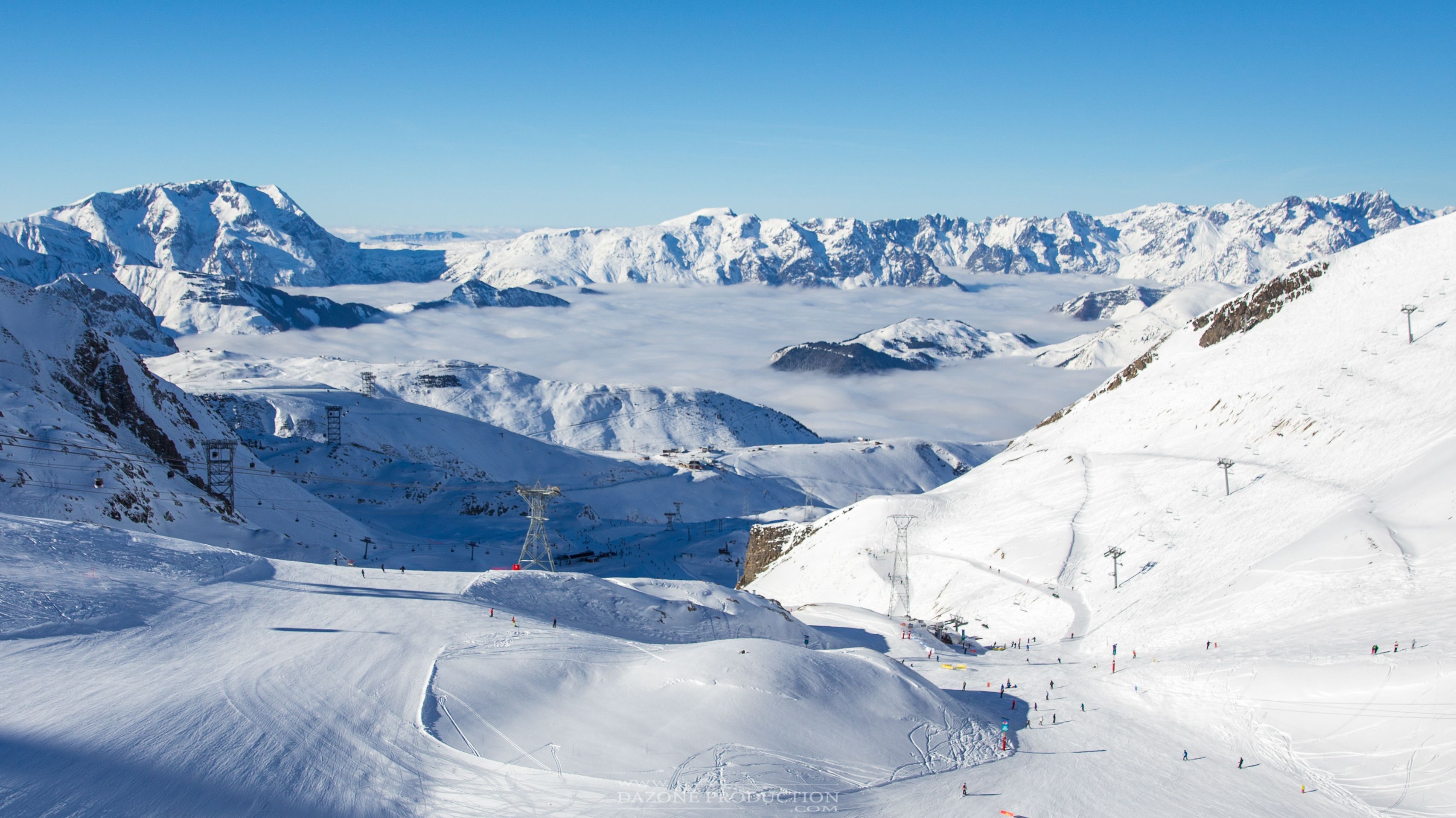 Paisaje montañoso cubierto de nieve con pistas de esquí y cielo despejado.