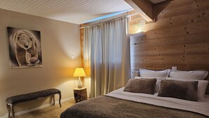 Een slaapkamer met een houten hoofdbord, een bed met meerdere kussens, een bankje, een schilderij en een lamp.