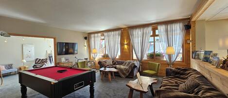 A cozy room with a pool table, comfortable seating, and large windows with curtains.