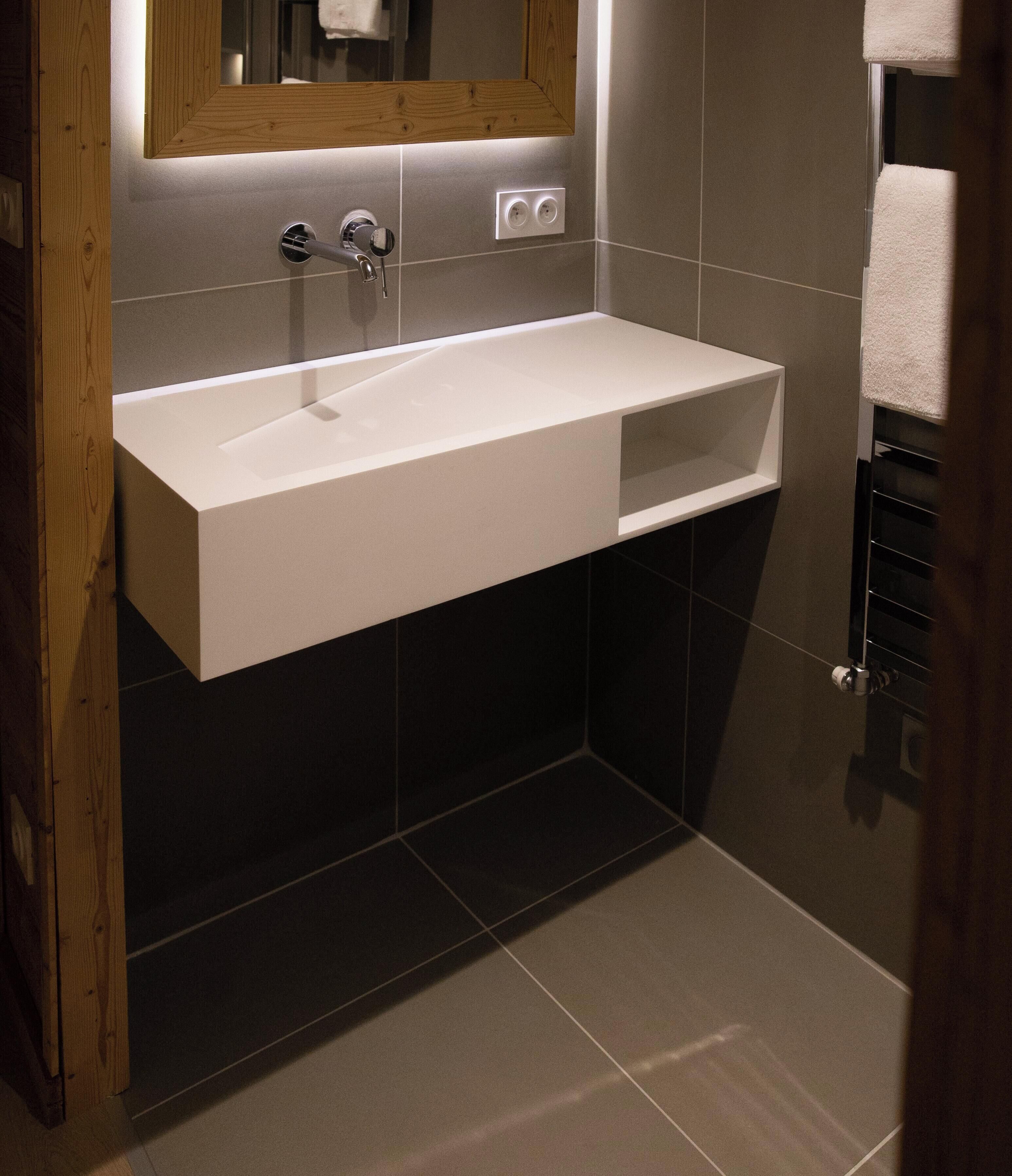 A modern bathroom with a white sink, dark tiles, and a wooden-framed mirror.