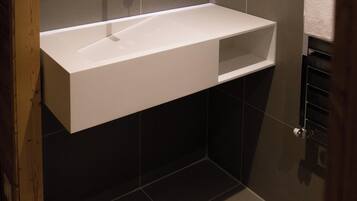 Un bagno moderno con un lavandino bianco, piastrelle scure e uno specchio con cornice in legno.