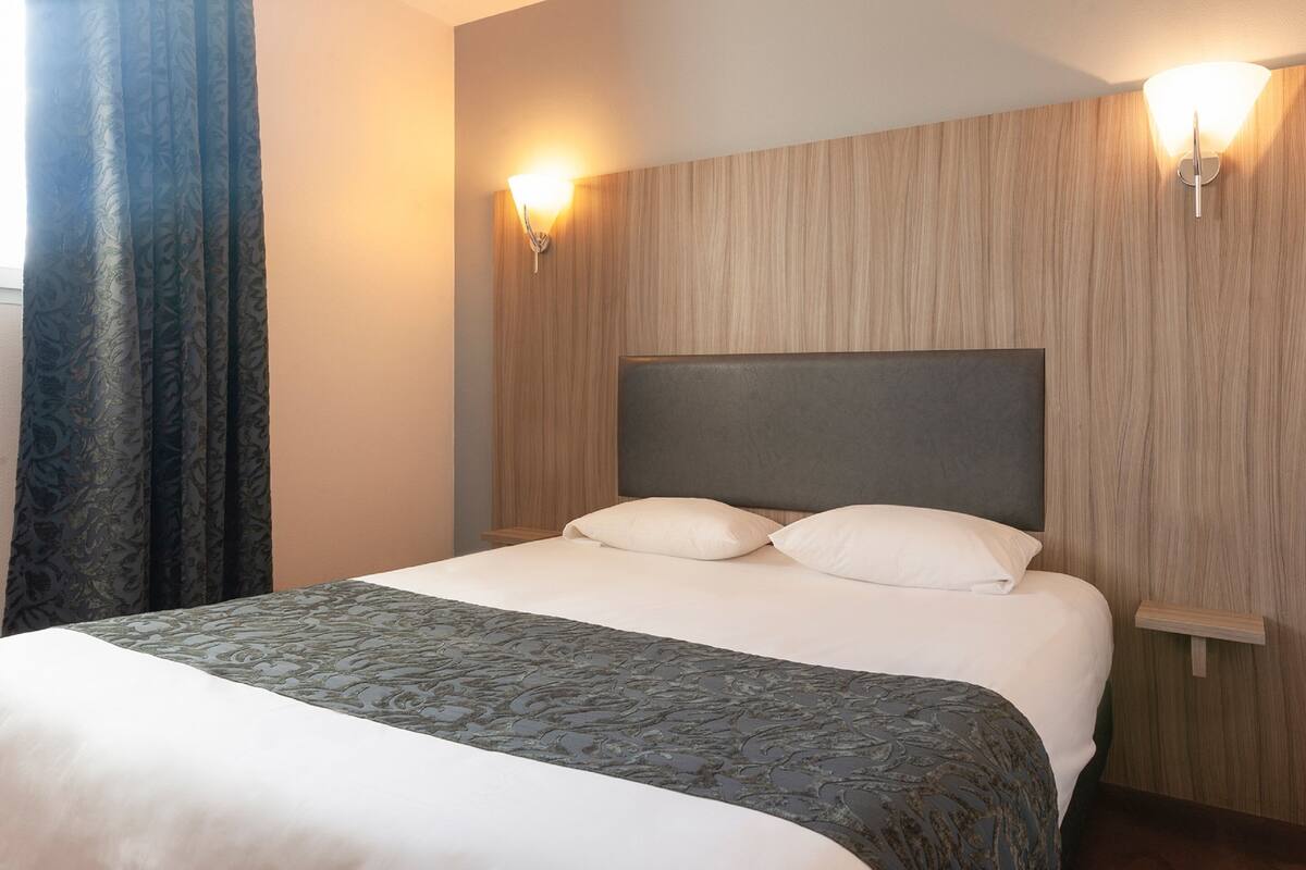 Una habitación de hotel con una cama grande, dos mesitas de noche y un cabecero.