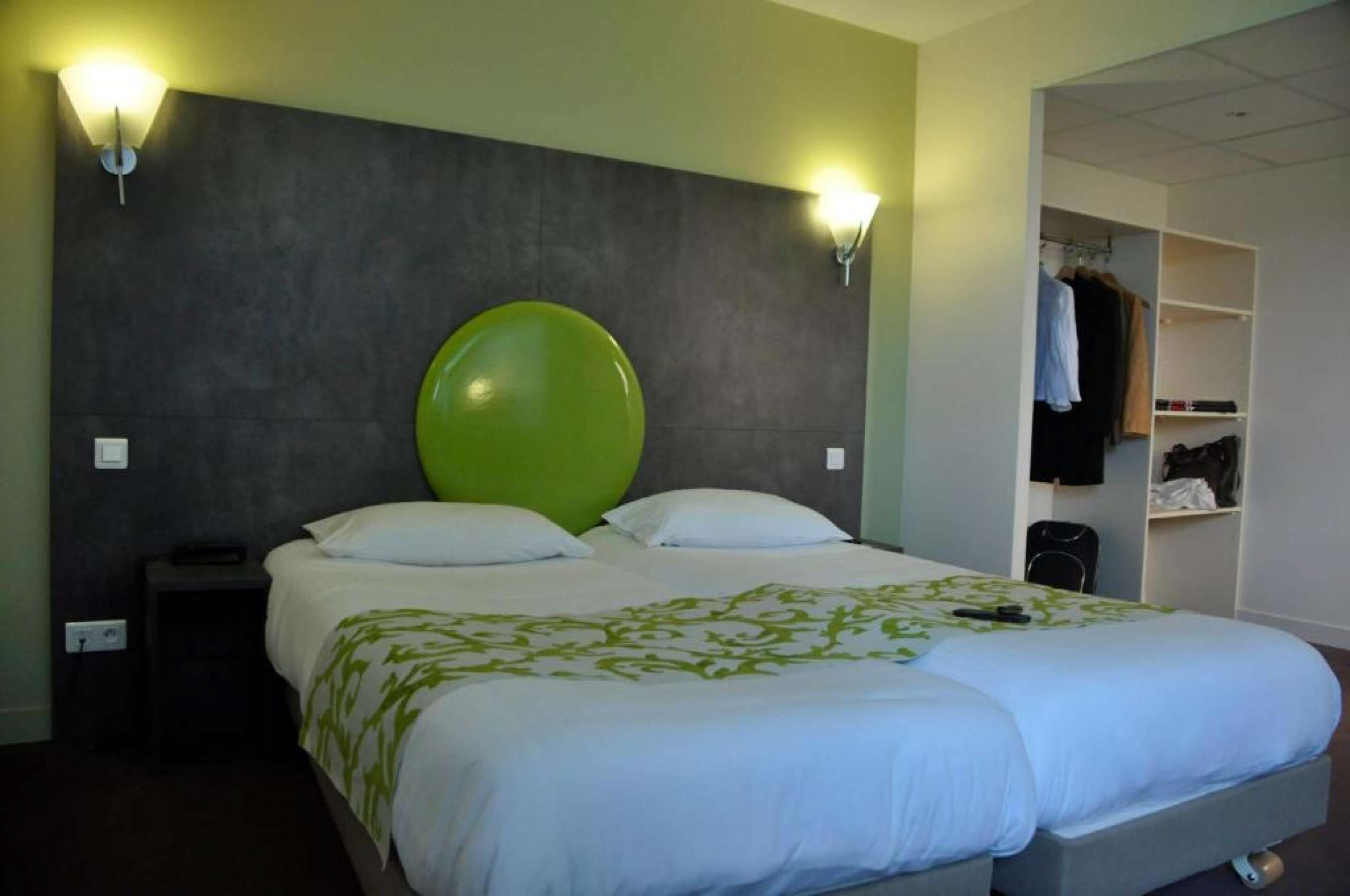 A hotel room with a large bed, two bedside lamps, a wardrobe, and a coat rack.