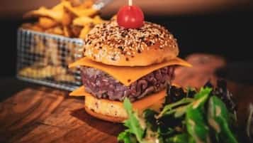 Una hamburguesa con pan de sésamo, una cereza encima y una guarnición de papas fritas sobre una mesa de madera.