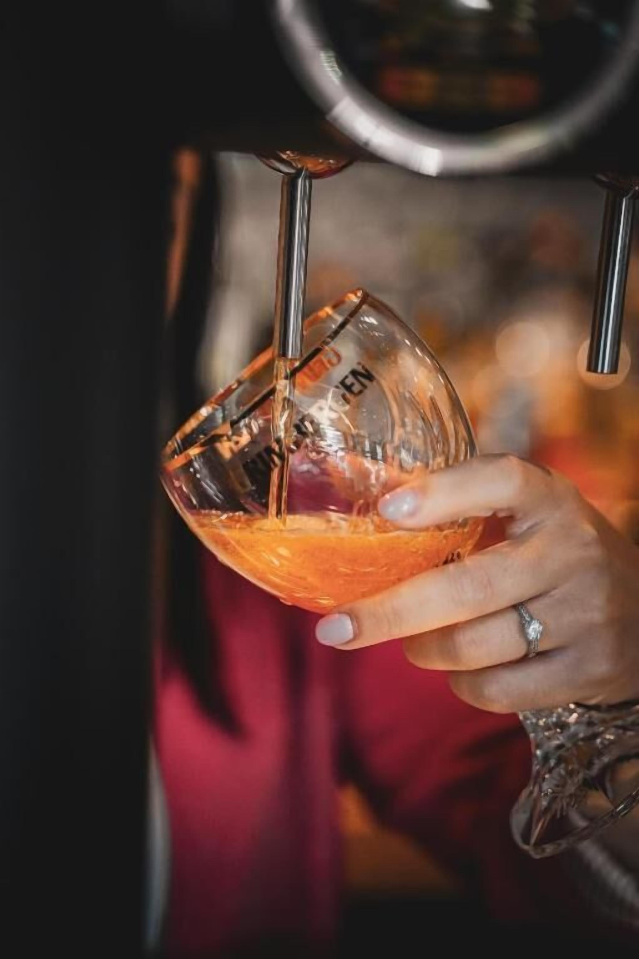 A hand holding a glass with a measurement marking, pouring a liquid from a tap.