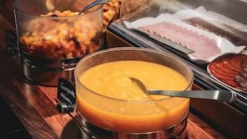 Un bufé con diversas opciones de comida, incluyendo un tazón de sopa, panes en cestas y recipientes con distintos alimentos.