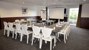 A conference room with a long table, white chairs, a projector screen, and a welcome banner. - Brit Hotel Confort Alexia La Souterraine (La Souterraine)
