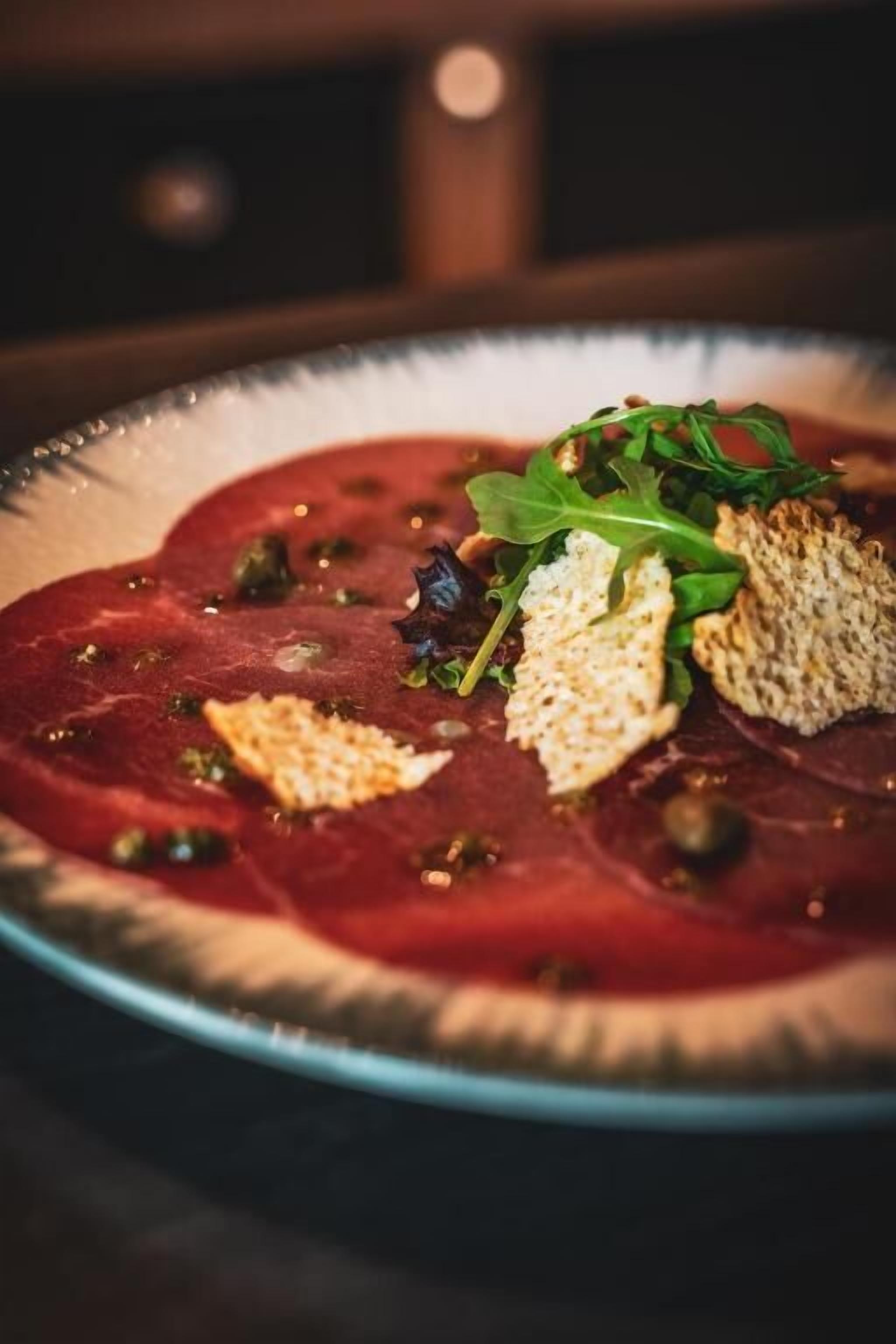 Un piatto di carne rossa affettata, guarnita con verdure fresche e crackers.