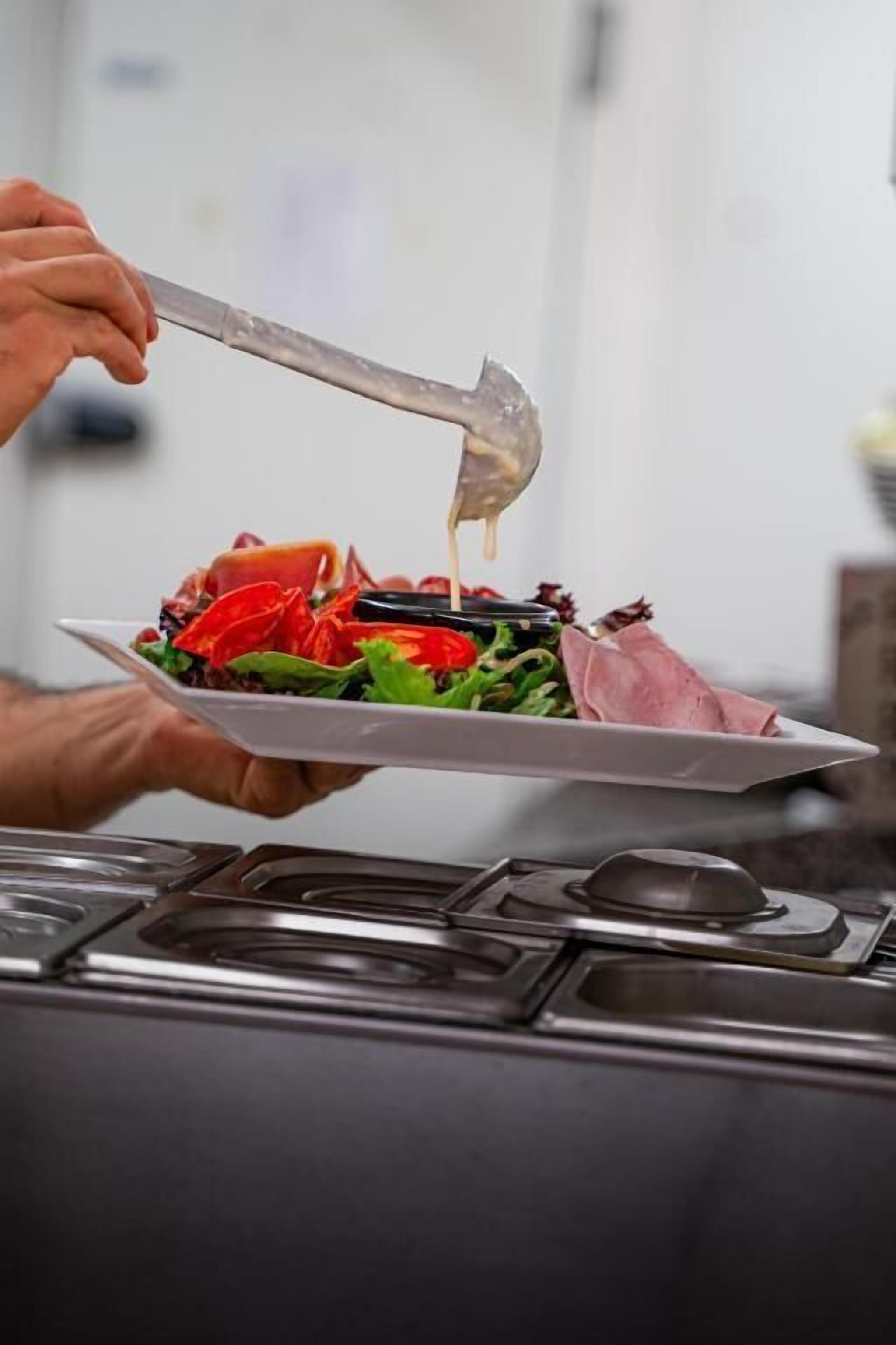 Una persona sosté un plat amb amanida i un ganivet.