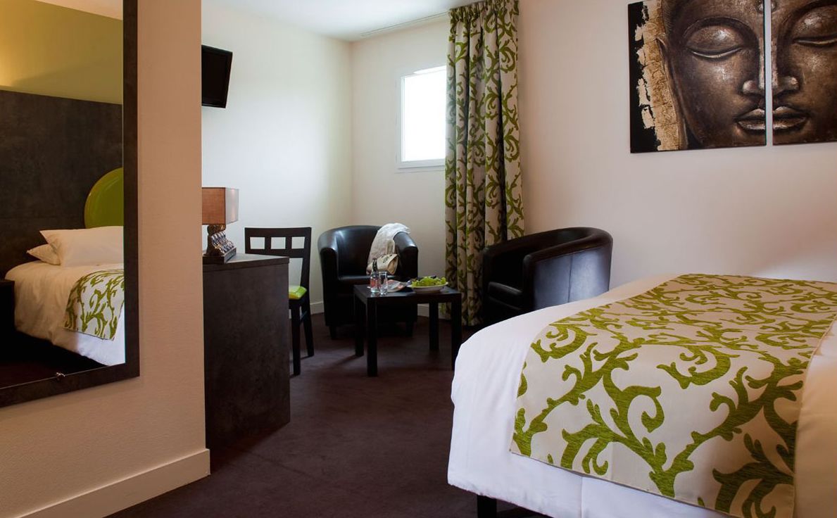 Habitación de hotel con cama, una silla, un escritorio, un espejo y un cuadro de Buda en la pared.