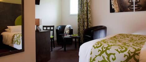 Habitación de hotel con cama, una silla, un escritorio, un espejo y un cuadro de Buda en la pared.