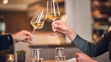 Zwei Personen stoßen mit Weingläsern an einem Tisch an, der mit Wassergläsern und einer Kerze bestückt ist, in einem schwach beleuchteten Restaurant.