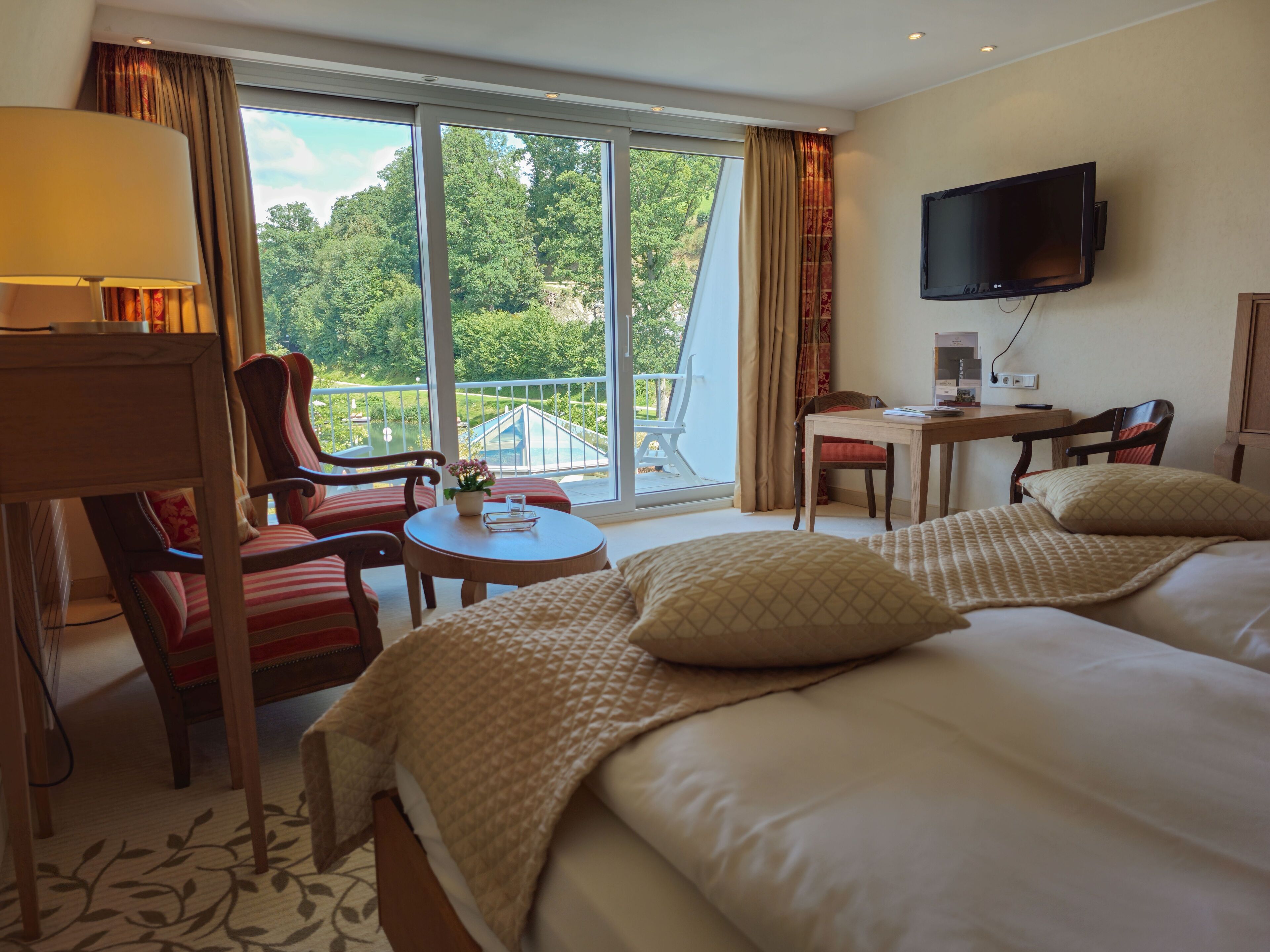 A hotel room with a balcony, a desk, a TV, and two beds.