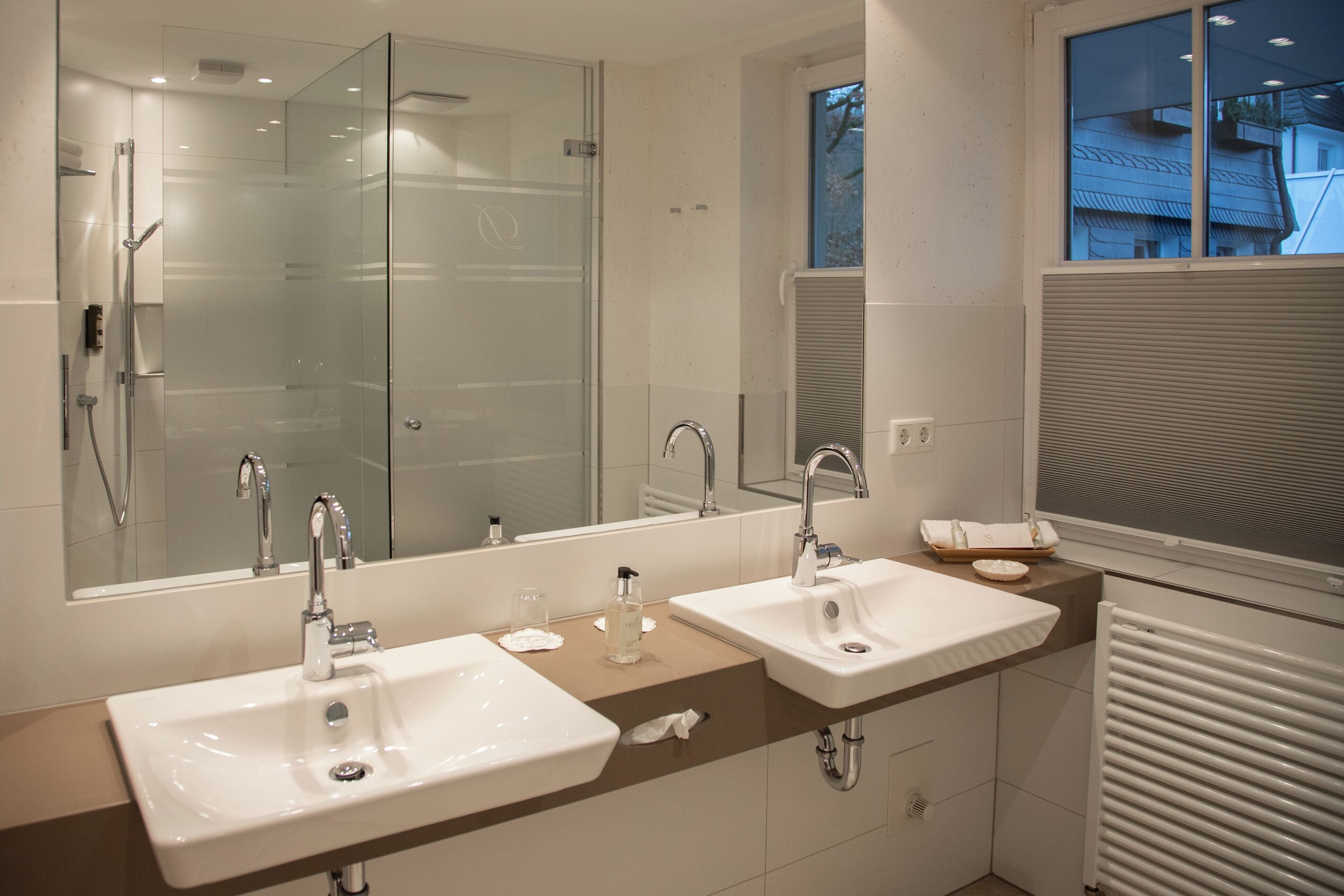 Un baño moderno con dos lavamanos, cabina de ducha con mampara de cristal y un espejo grande.