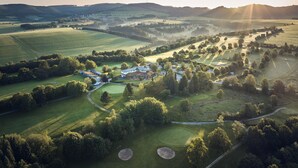 An aerial view of a golf course with a clubhouse, surrounded by rolling hills and open fields. - Hotel Deimann (Schmallenberg)