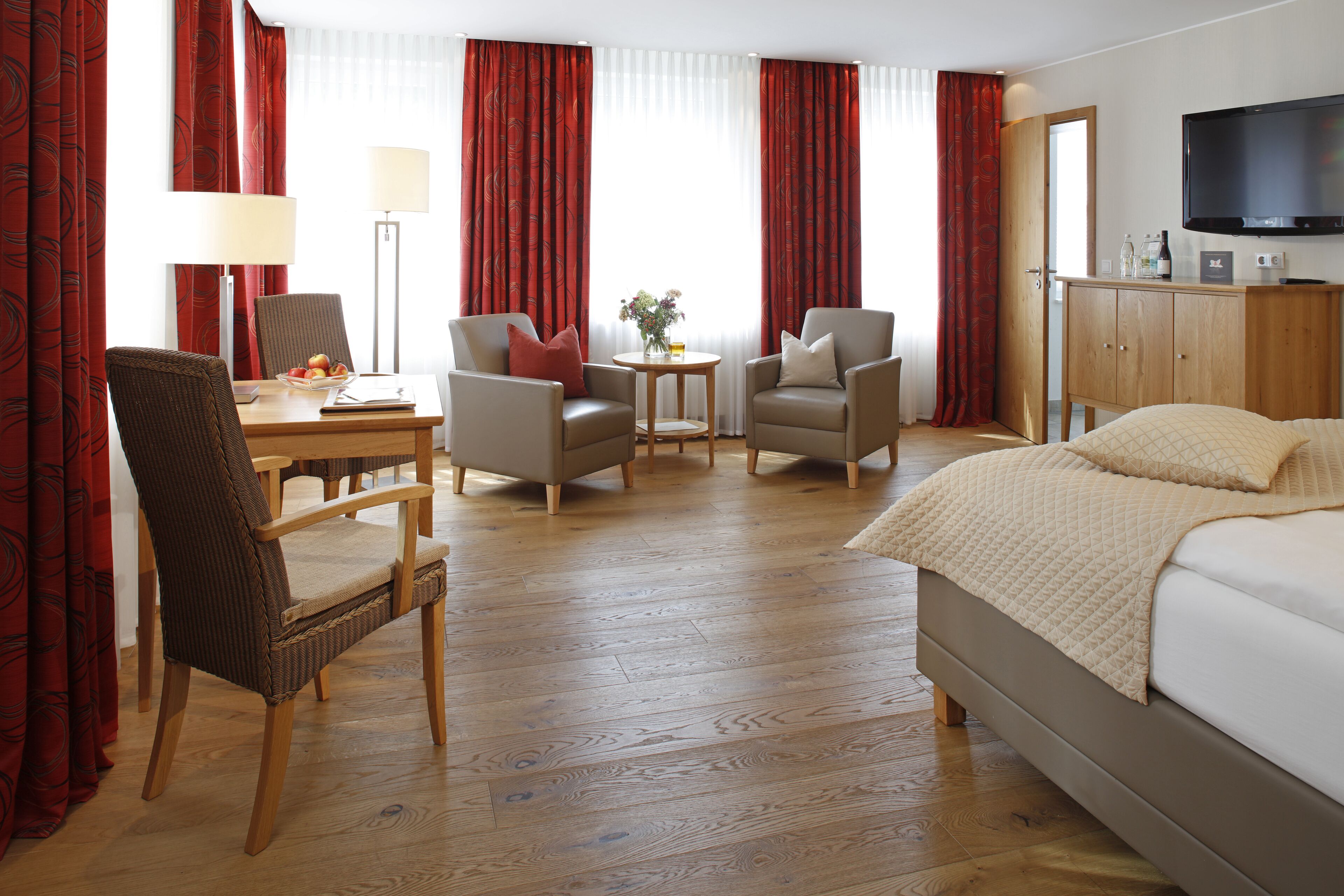 Ein Hotelzimmer mit einem Bett, zwei Sesseln, einem Schreibtisch mit Lampe, einem Fernseher und einem Holzschrank.