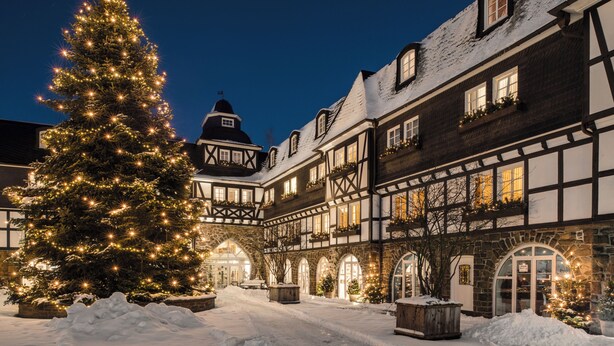 A traditional half-timbered building with a snow-covered courtyard and a large Christmas tree adorned with lights. - Hotel Deimann (Schmallenberg)