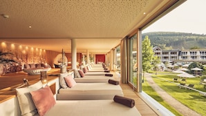A spa area with multiple massage tables arranged in a row, a reception desk, and a view of the hotel and surrounding landscape. - Hotel Deimann (Schmallenberg)